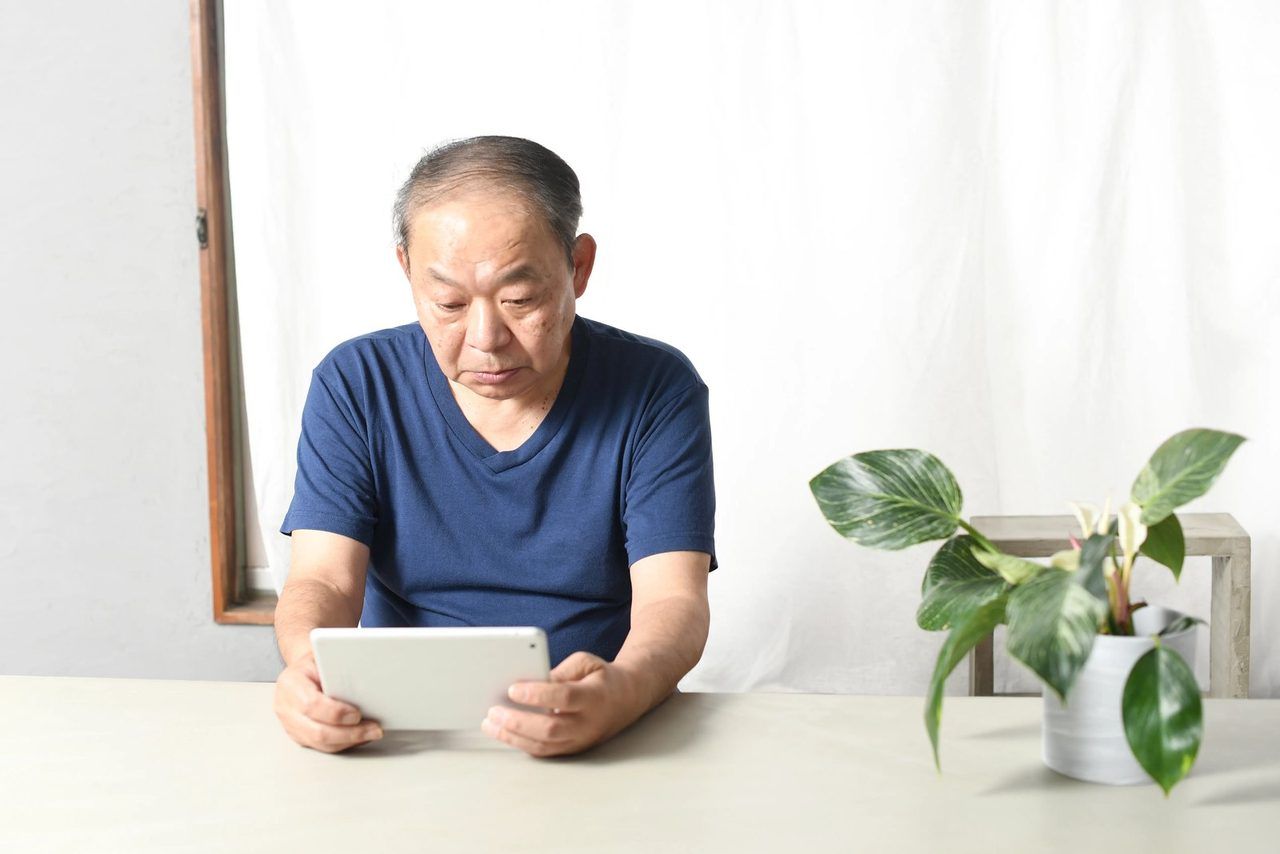 タブレットを見ながら、考えるご高齢の男性