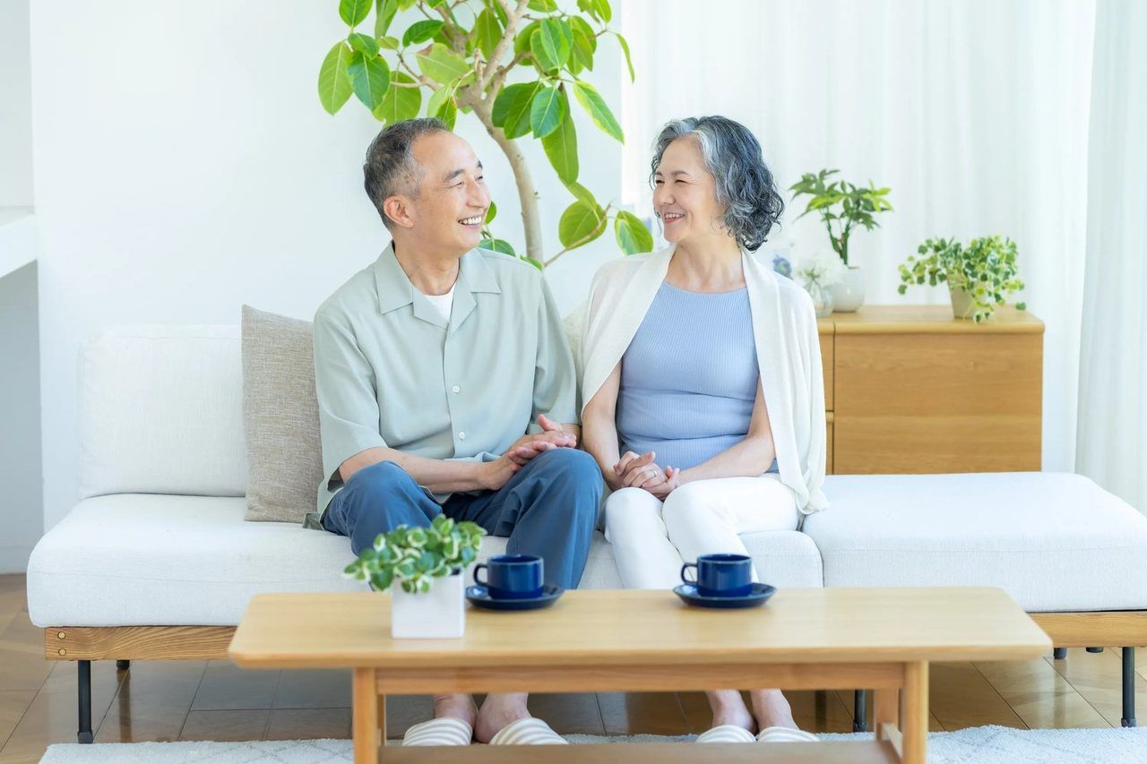 ソファに並んで座り、笑顔で顔を見合わせるご高齢のご夫婦