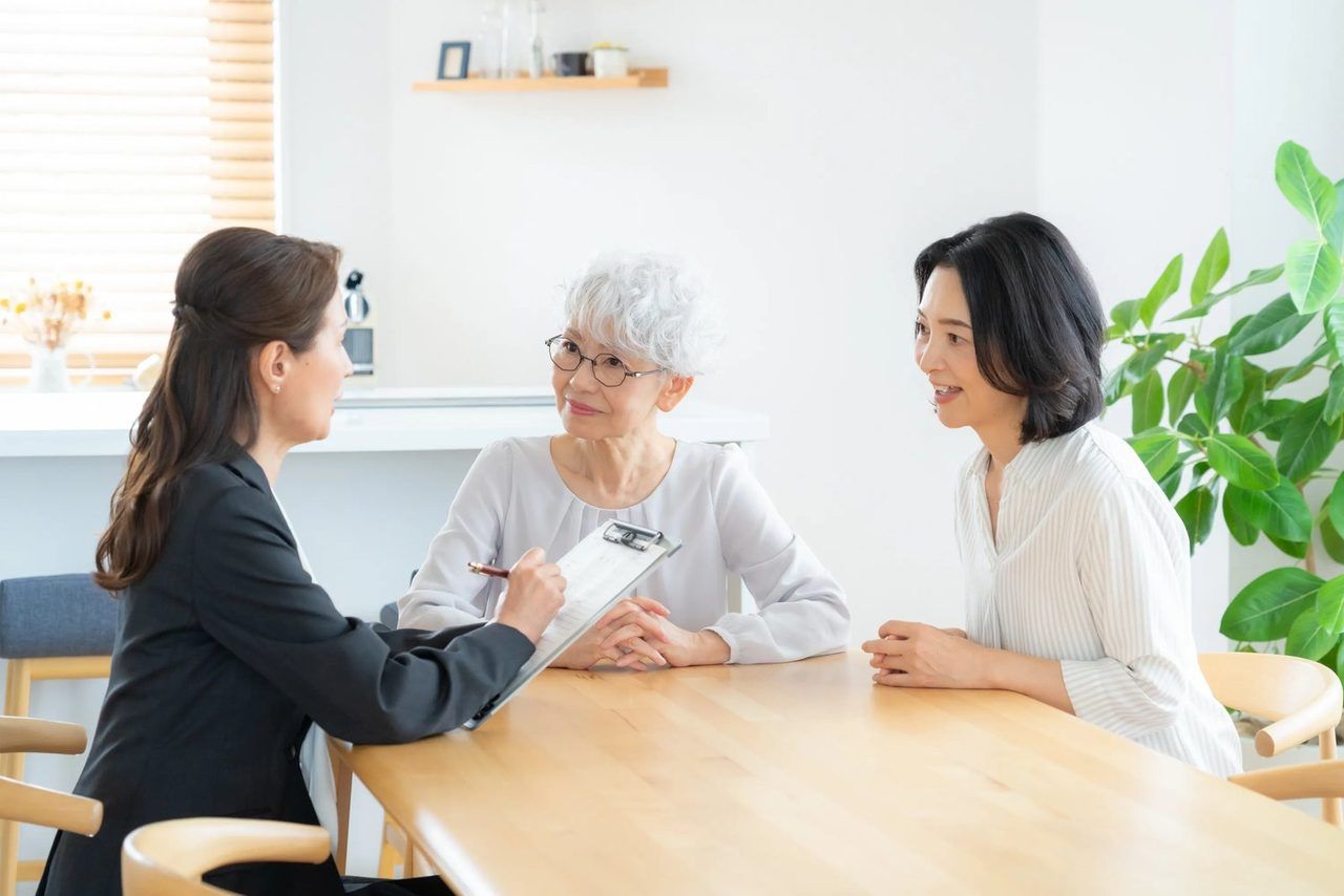 女性スタッフが、ご高齢の女性とそのご家族の話を、メモを取りながら聞いている場面